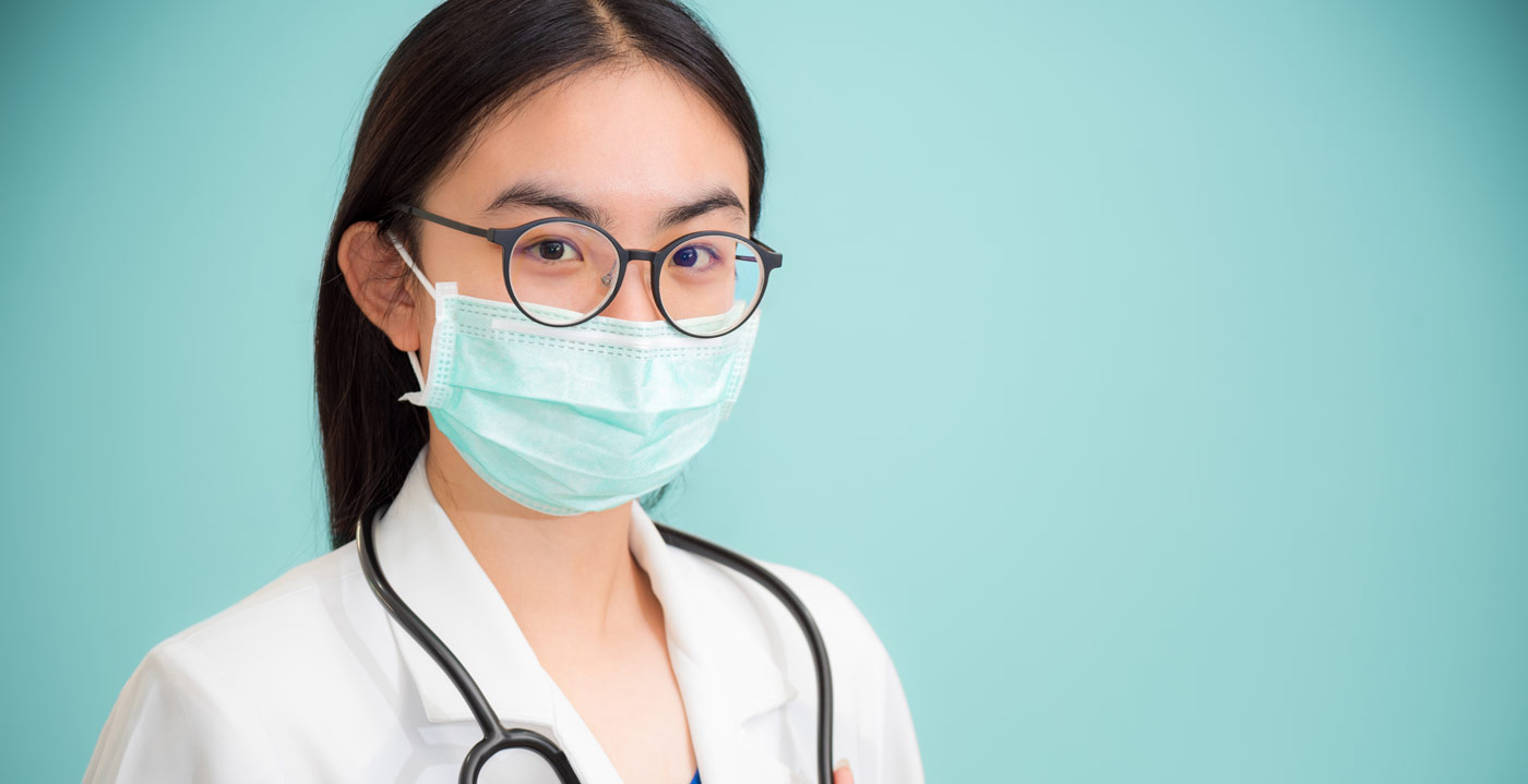 A doctor poses with their stethoscope and glasses and a mask.