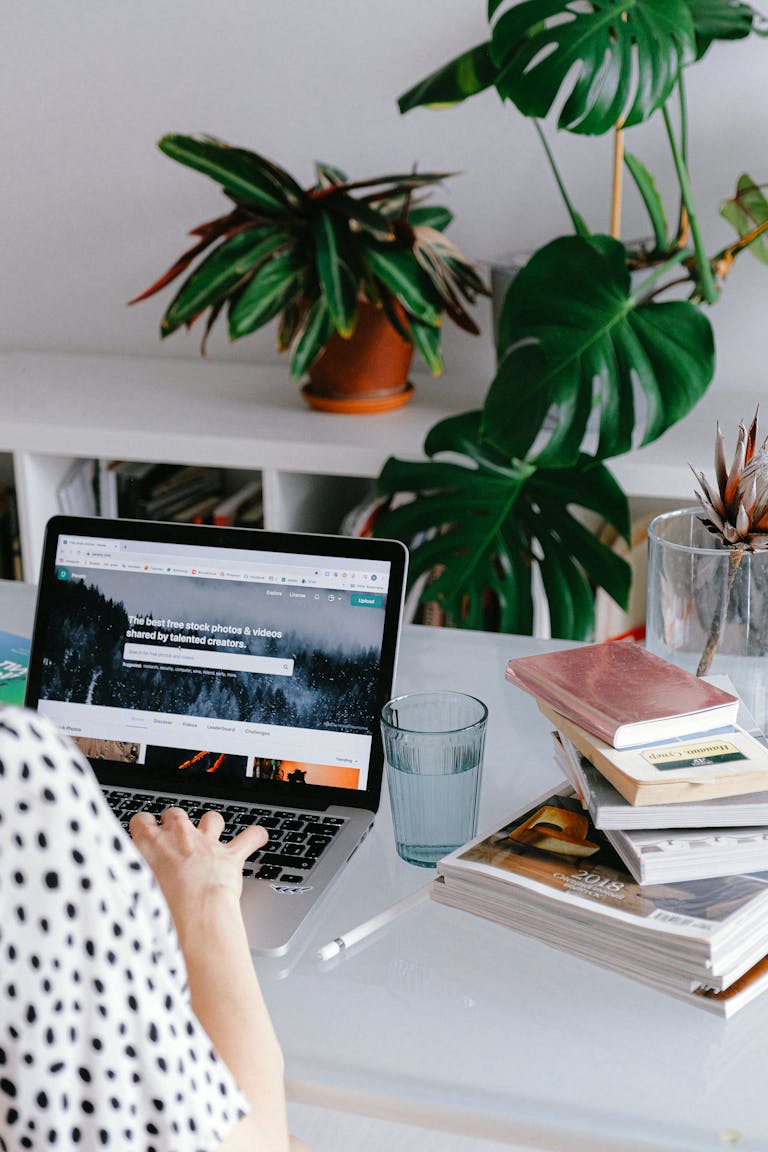 A person working from home on teir laptop surrounded by plants and books for a cozy office feel.